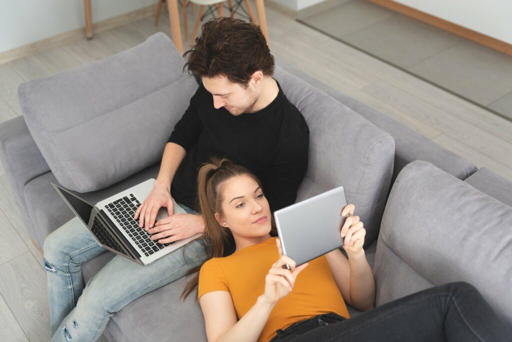 couple on couch using home internet on laptop and tablet